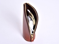 職人手作皮革直立式收納筆袋，呈現自然的棕色皮革質感，拉鍊為金色。袋內裝有白色充電器和淡黃色充電線。