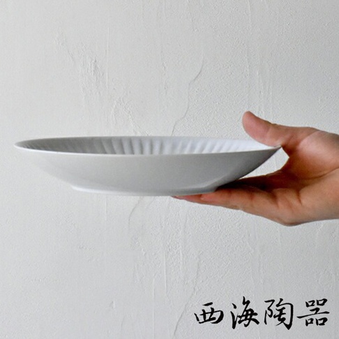 一只手托著一個淺灰色、帶有放射狀壓紋的陶瓷主食盤。