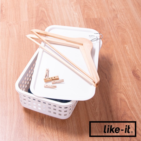 白色網格設計的塑料洗衣提籃，內有衣物，上方疊放著白色蓋子，蓋子上放有幾件木質衣架和夾子。