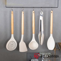 五件白色矽膠廚房用具，包含漏勺、鍋鏟、湯勺、夾子和飯勺，皆配有木質手柄，懸掛於黑色收納架上。