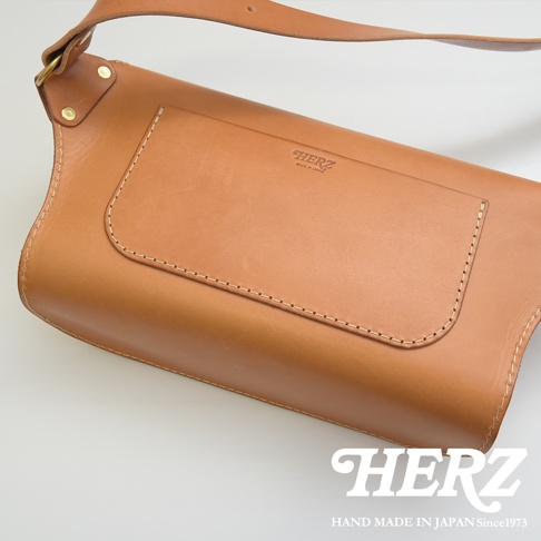 職人手作皮革立體斜背包，呈現自然棕色皮革，包身結構立體，正面設有翻蓋式口袋，以明線縫製，皮革質感良好，搭配金屬扣環與寬版背帶。