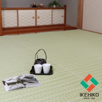 淺綠色水洗PP材質的榻榻米風格地墊，表面有細密的菱形紋理，鋪設於木質地板上。畫面前景有一本打開的雜誌，上方擺放著一個黑色托盤，托盤上有兩個白色杯子和一個竹編提籃。