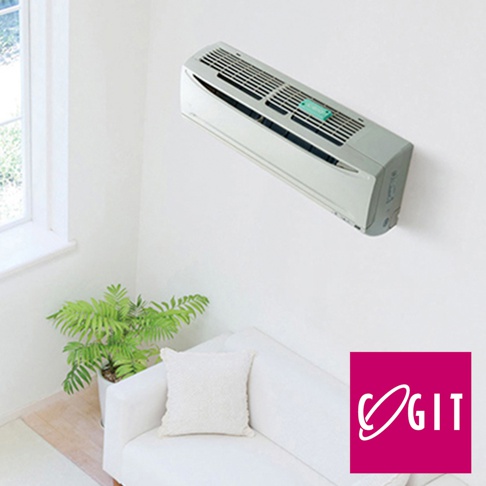 一台淺灰色壁掛式冷氣機安裝在白色牆壁上，冷氣機下方有一張白色沙發、一個白色抱枕和一盆綠葉植物。