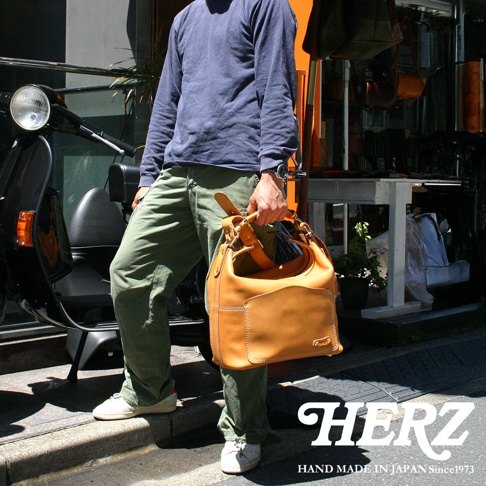 職人手作厚實皮革單肩波士頓包，呈現溫潤的焦糖色澤，皮革表面有自然紋理，包身設計簡潔，搭配可調節的皮革提把，適合日常攜帶。