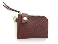 職人手作的深棕色皮革短夾，帶有獅鬃般的紋理，拉鍊開合，配有黃銅按扣、皮革拉帶及金屬D型環。