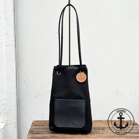 神戶clueto 黑色尼龍束口肩背包，正面有義大利皮革小口袋，掛有品牌圓形皮革吊飾