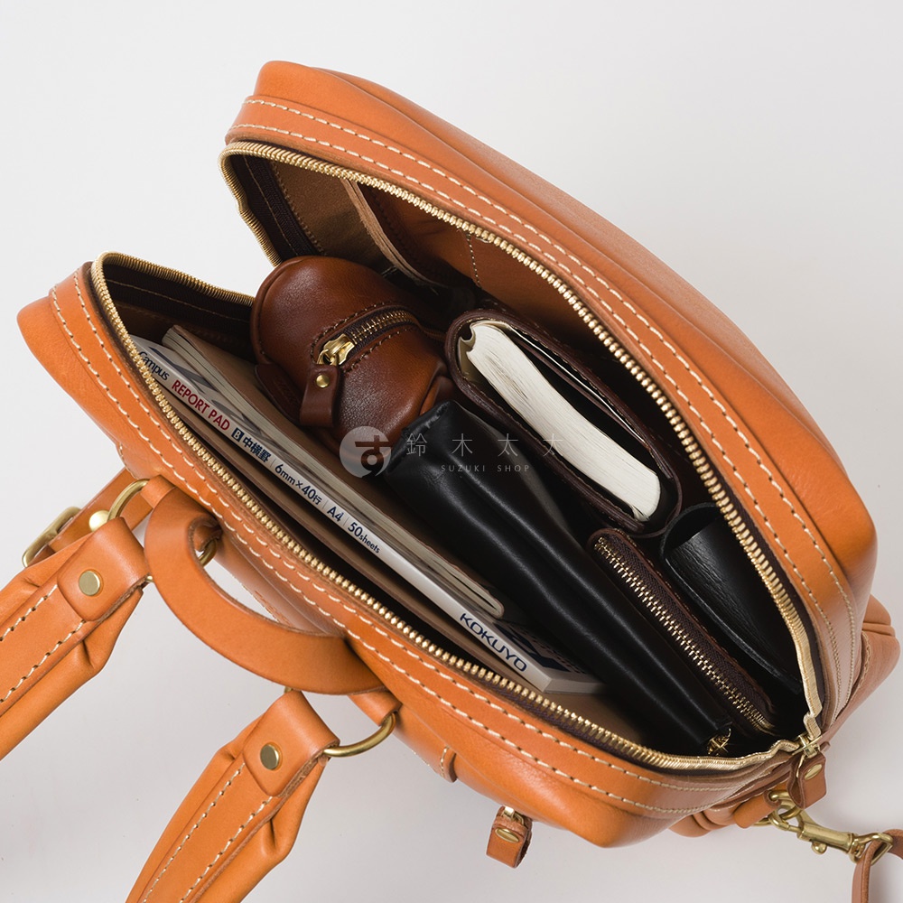 棕褐色皮革商務後背包，內部裝有筆記本、錢包、文件夾和一個小皮革零錢包。