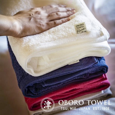 疊放的三條細纖浴巾，分別為白色、海軍藍及桃紅色。白色浴巾上有一隻手，並有「OBORO TOWEL Kiwami EST. 1908」的標籤。