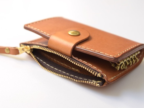 一個棕褐色全皮革拉鍊零錢鑰匙包，帶有黃銅色拉鍊和四個鑰匙鉤，以及一個鈕扣開合。