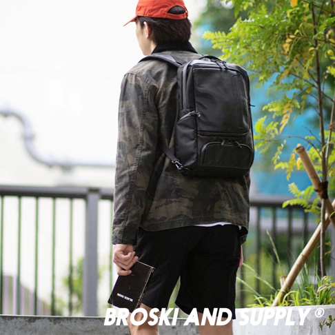 身穿迷彩外套的男性背著黑色防水真皮革兩用手提後背包，背包有兩個前袋和一個主隔層。