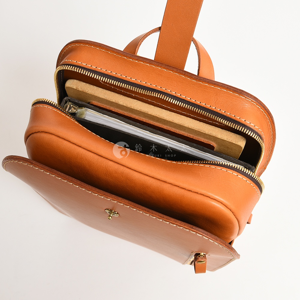 職人手作皮革後背包，呈現自然棕色，主隔層敞開，內有筆記本和文件夾，展示精緻縫線與金色拉鍊。