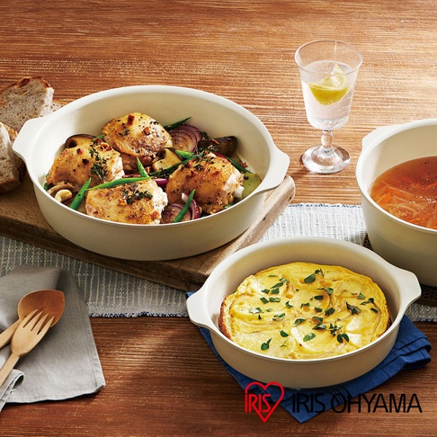 一組乳白色可拆式陶瓷不沾平底鍋，其中一個鍋內盛有烤雞和蔬菜，另一鍋內有馬鈴薯烘蛋，桌上還有玻璃杯和木製餐具。