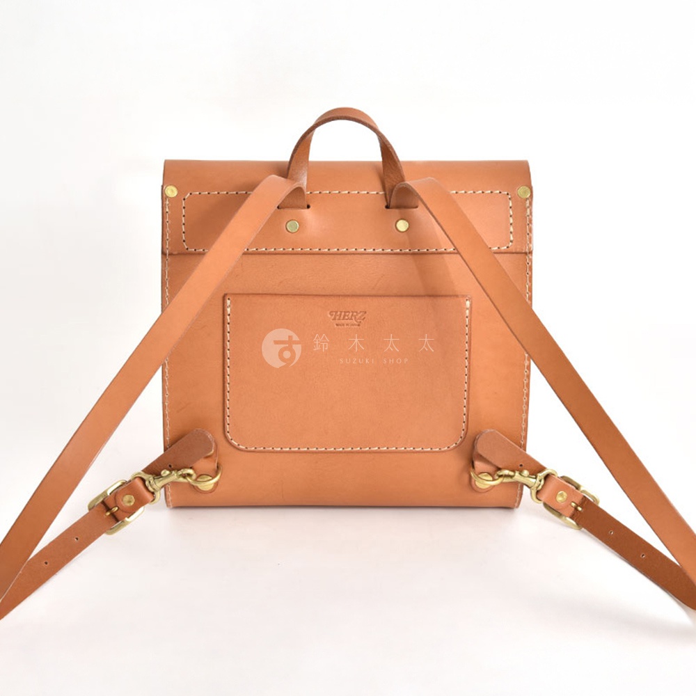 職人手作皮革翻蓋迷你後背包，經典棕色，採用天然皮革製作，帶有兩個可調節肩帶和金屬扣環，後方有一個貼袋，印有品牌標誌。