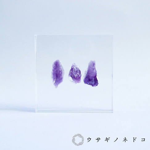 透明壓克力方塊中，有三塊不規則形狀的紫色紫水晶原礦，水晶表面呈現天然紋理。