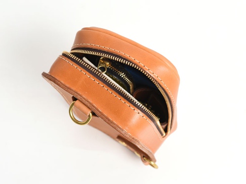 職人手作皮革兩用直立型斜背包，呈現天然棕色，以堅韌皮革製成，設有黃銅拉鍊和 D 型環。包包開口處可見內部藍色內襯及部分物品。