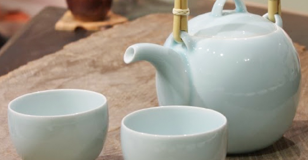 淡藍色陶瓷壺杯組，壺身圓潤，配有竹製提把，兩個同色系的茶杯擺放在壺旁，整體呈現簡約日式風格。