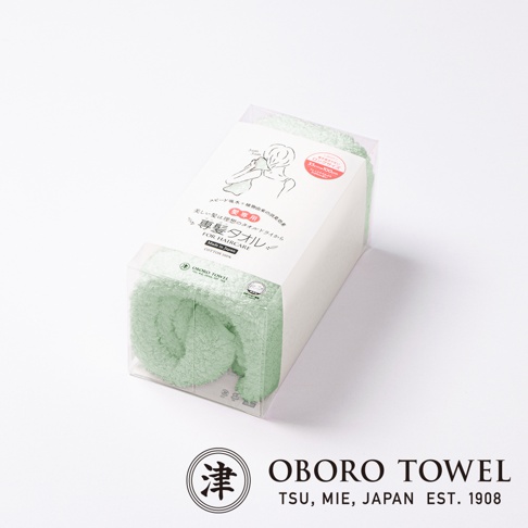 綠色毛巾，材質為棉，包裝盒上有日文說明及簡單圖案，產品品牌為 OROBO TOWEL。