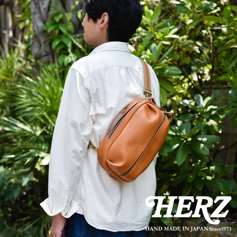模式B： 日本HERZ手工皮革立體運動斜背包，揹在一位男士背後，斜背包為棕褐色，採用職人手作工藝。