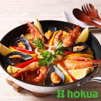 黑色輕量炒鍋內盛滿色彩豐富的海鮮飯，有鮮紅的蝦、黑色的淡菜、黃色的甜椒，以及點綴的檸檬片和歐芹。