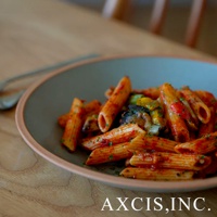 素燒陶瓷義大利麵盤盛裝著筆管麵，淋上紅醬並拌有蔬菜丁，盤緣呈現大地色調。