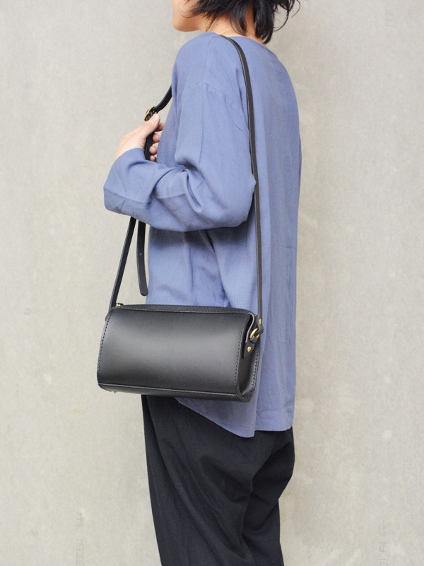 黑色皮革拉鍊單肩包，圓筒狀包身，金色五金配件，配有可調節的細肩帶。