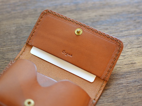 職人手作的棕色皮革Organ名片夾，內部可見一個白色名片，皮革表面壓印有「Organ」字樣，並有金色按扣。