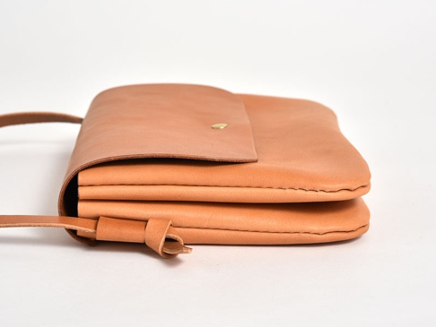 職人手作皮革橫式隨行袋 (CP-9)，採用天然皮革材質，呈現柔和的淺棕色。袋子設計簡潔，以側邊視角呈現，可見其厚實的皮革層疊，並配有細長的皮革背帶，背帶與袋身以皮革繩結固定。