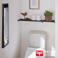 黑桿全功能伸縮置物架，安裝在白色牆面上，架上擺放有兩個衛生紙捲、一個木製裝飾鳥、一小盆綠色植物。下方為白色馬桶，右下角為品牌 Logo。