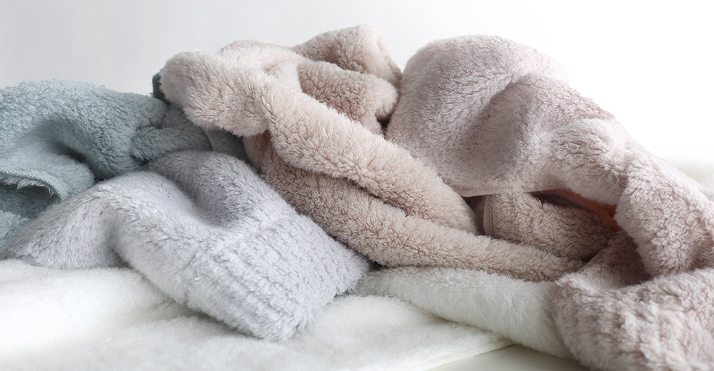 一堆柔軟的毛絨布料，有淺藍色、淺灰色、粉色和白色，堆疊在一起，背景是白色。