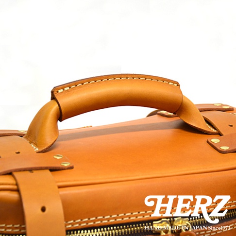 職人手作皮革大型三用旅行後背包 A-21，特寫展示包款的頂部提把及部分箱身，以質感棕色皮革製成，細緻車縫線與金屬銅釦點綴，展現精湛工藝。