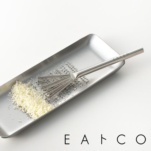日製料理小刷，銀色不鏽鋼材質，刷頭呈扇形，搭配細密的金屬絲，用於處理食材。產品置於同材質的長方形托盤中，托盤內有少量刨絲的白色食材。