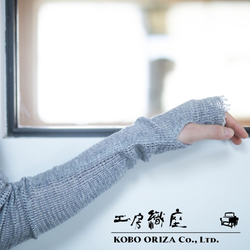 一隻手臂佩戴著淺灰色、網狀織紋的MOJIRI NECK’ｍ輕柔有機棉遮陽袖套，袖套具有指洞設計，材質輕薄透氣，邊緣有流蘇裝飾。