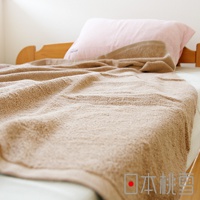 一張淺棕色超大浴巾覆蓋在床上，浴巾質地蓬鬆柔軟，局部有皺褶。床頭有一顆粉紅色枕頭，床架為木質。