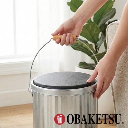 OBAKETSU 手工製銀色凳子儲物桶，頂部有黑色坐墊，附有方便搬運的木質手柄。