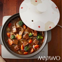 陶土湯鍋內盛有燉牛肉、胡蘿蔔塊、花椰菜和洋蔥，搭配白色鍋蓋，鍋蓋飾有金色放射狀圖案和紅色小花。