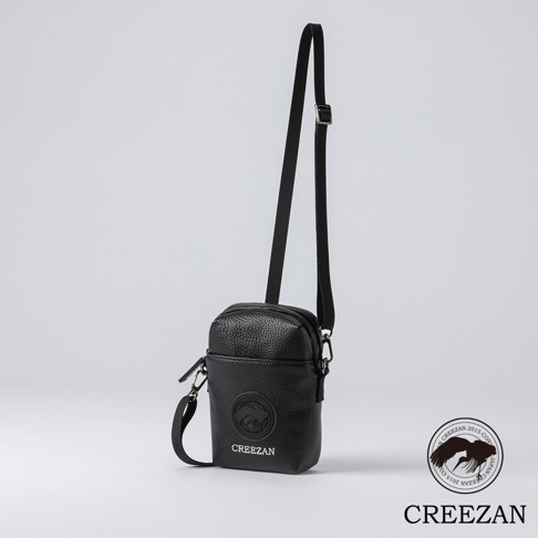 黑色皮革迷你側背收納包，正面有圓形壓紋品牌標誌與品牌名稱「CREEZAN」，附有可調式斜背帶。