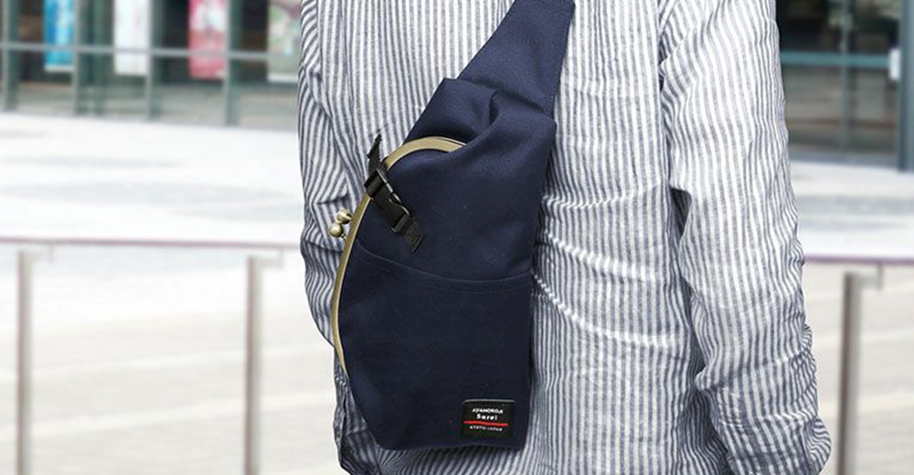 以斜背方式穿著一件條紋襯衫的單肩包，包包為海軍藍色，附有金色搭扣和黑色調節帶。