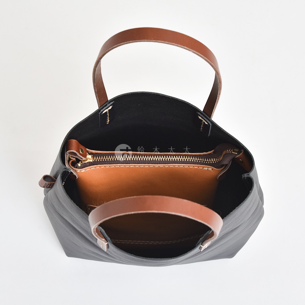 職人手作皮革直式隨身單肩包，黑色皮革包體，內部有一個棕色皮革拉鍊夾層，搭配棕色皮革提把。