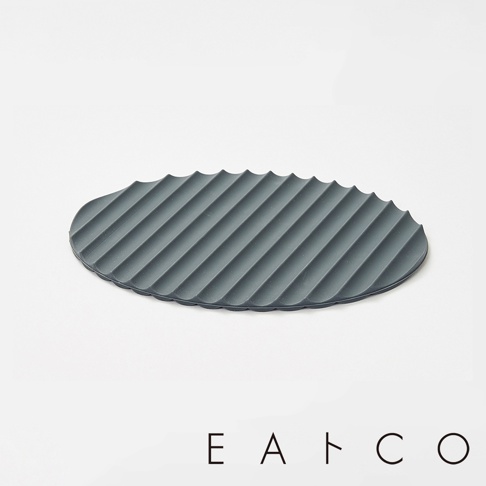 深灰色矽膠隔熱墊，表面有規則的波浪紋路，邊緣呈鋸齒狀，橢圓形設計。