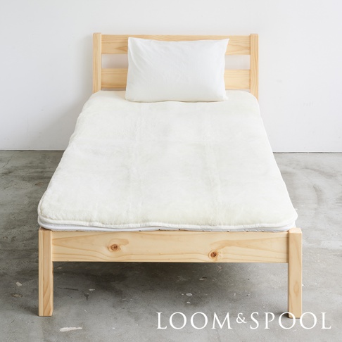 單人床架上鋪著厚實的白色美麗諾羊毛保暖墊，墊上有一顆白色枕頭。