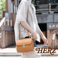 職人手作皮革復古杜勒斯手提包，採用天然棕色皮革製成，配有圓形提把、可調節斜背帶及金色鎖扣，包身線條俐落，復古風格明顯。