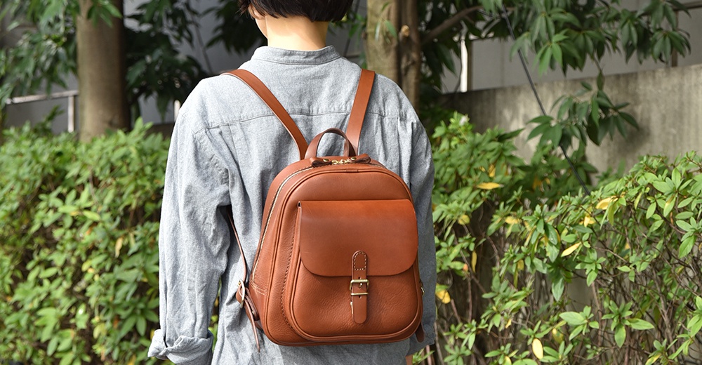 棕色皮革迷你後背包，具有立體前袋、金屬扣環和拉鍊開合，搭配皮革肩帶。