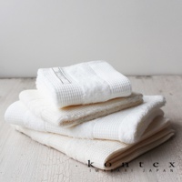 堆疊的今治雙織有機棉毛巾，有白色和米白色兩色，表面有鬆餅紋理，其中一條白色毛巾頂部有品牌標籤。