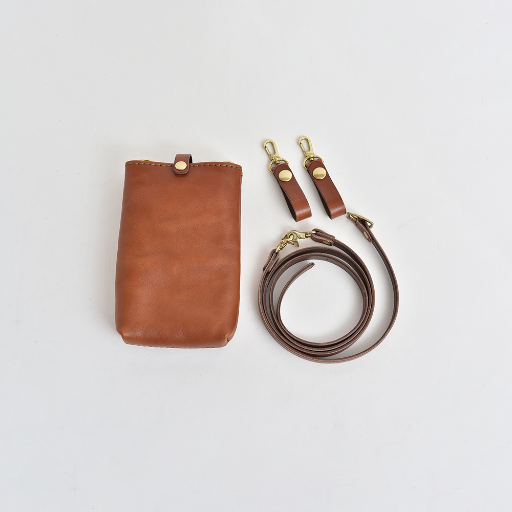 棕色皮革手機包，附有兩個獨立的皮革掛繩扣環和一條可拆卸的皮革斜背包帶，配有黃銅金屬配件。