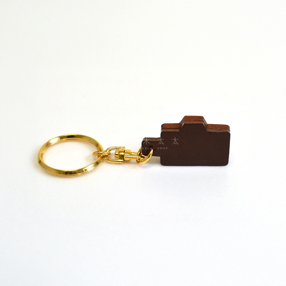 深棕色皮革製成的相機造型鑰匙圈，搭配金色金屬環與扣環。