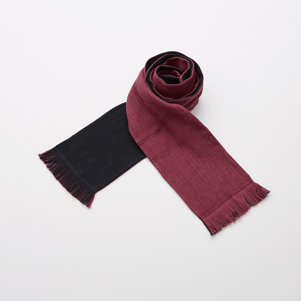 今治匹馬棉雙色圍巾，一端為黑色，另一端為酒紅色，兩色皆有流蘇，材質柔軟，圍巾捲起呈現螺旋狀。