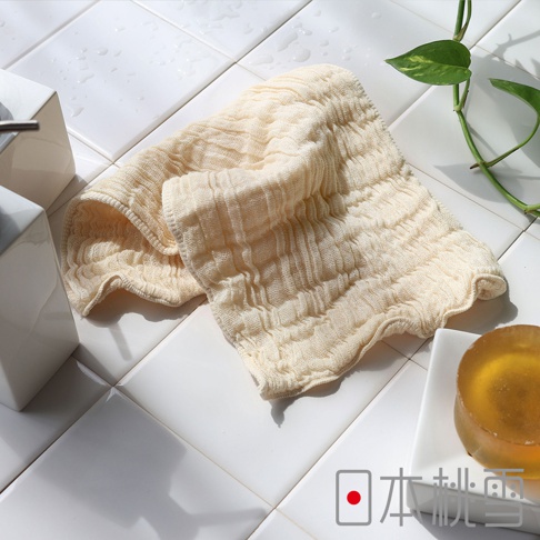日本桃雪立體褶皺柔綿紗布洗臉巾，搭配方形皂用於清潔，背景為白色磁磚，有綠色植物裝飾