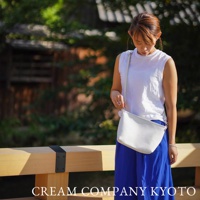 一名女性手持白色皮革隨身側背包，包包側邊有一個銀色U形拉鍊，肩帶為淺灰色。