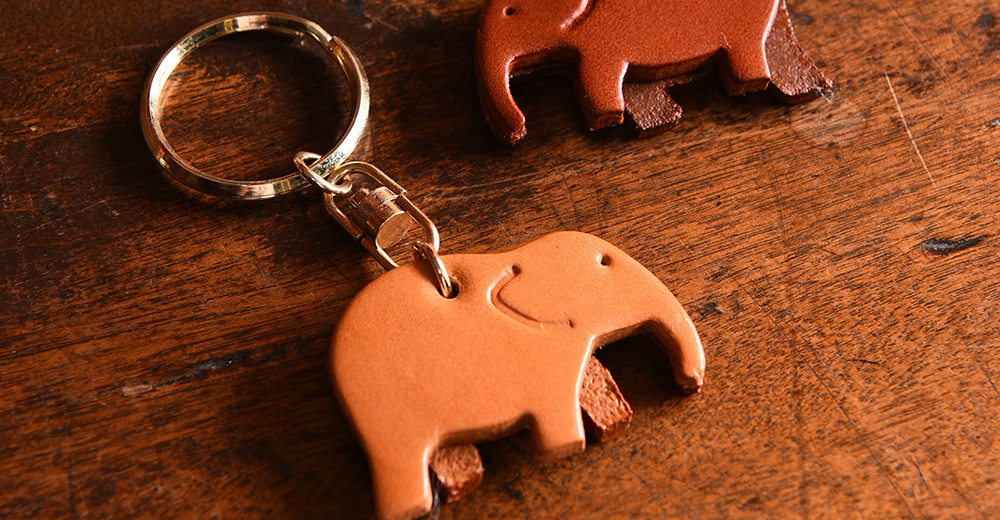 咖啡色皮革製成的大象造型鑰匙圈，附有金色金屬鑰匙環，另有一隻深棕色皮革大象鑰匙圈。