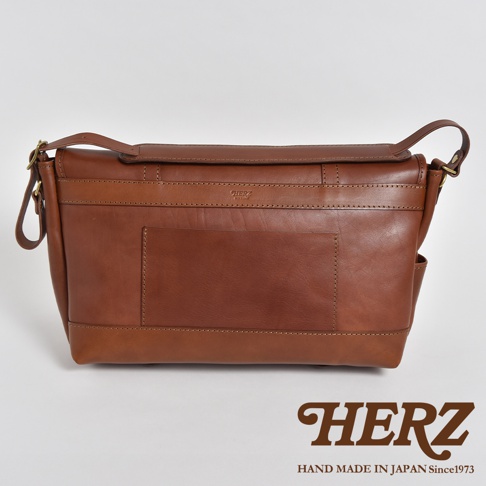 職人手作皮革復古郵差包，採用鞣製皮革製作，呈現溫潤的棕色調。包款設計簡潔，帶有翻蓋式開口，前方設有一體成形的方形貼袋，整體風格復古耐看。